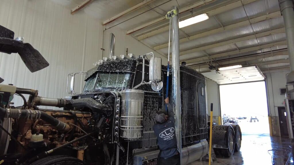 photo of a worker at ALE Truck Beds' truck wash cleaning one of the pipes with a brush at the end of a long handle.